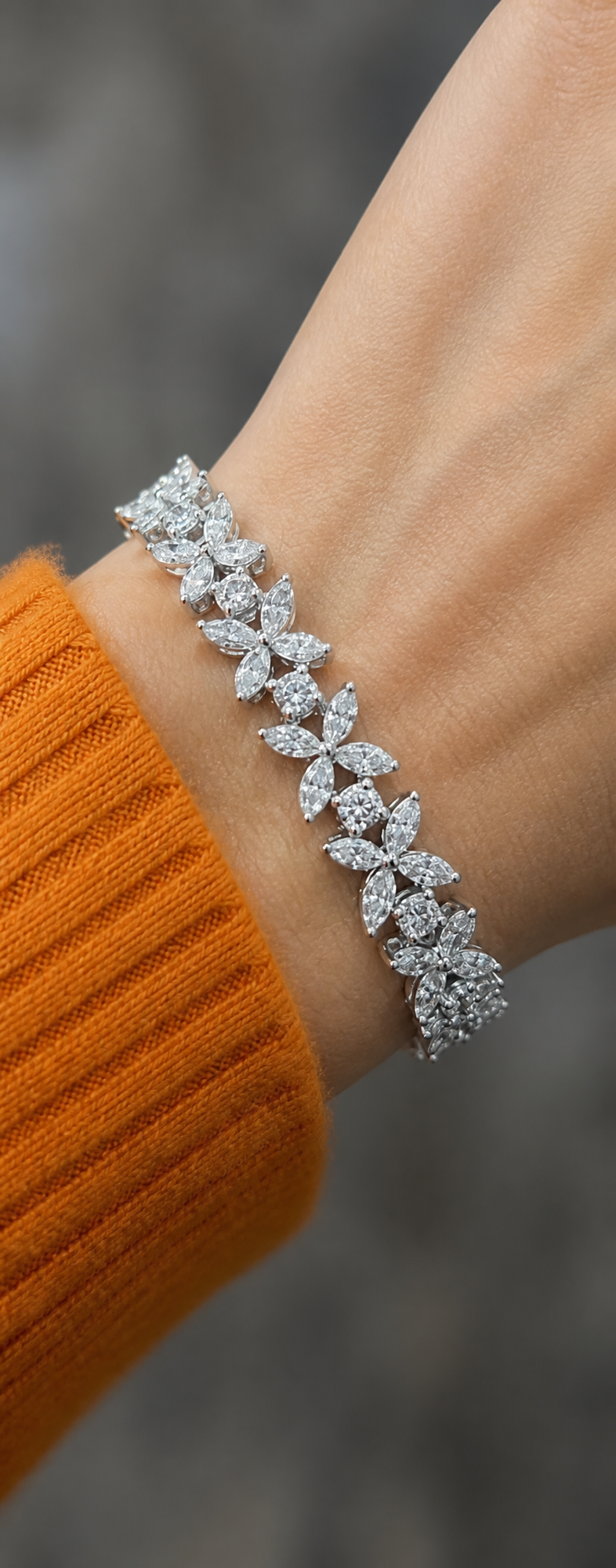 Diamond flower-motif bracelet worn on a wrist over an orange sweater